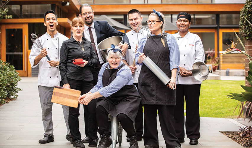 Image of the amazing kitchen team at the residential college posing with all the kitchen tools and having fun.